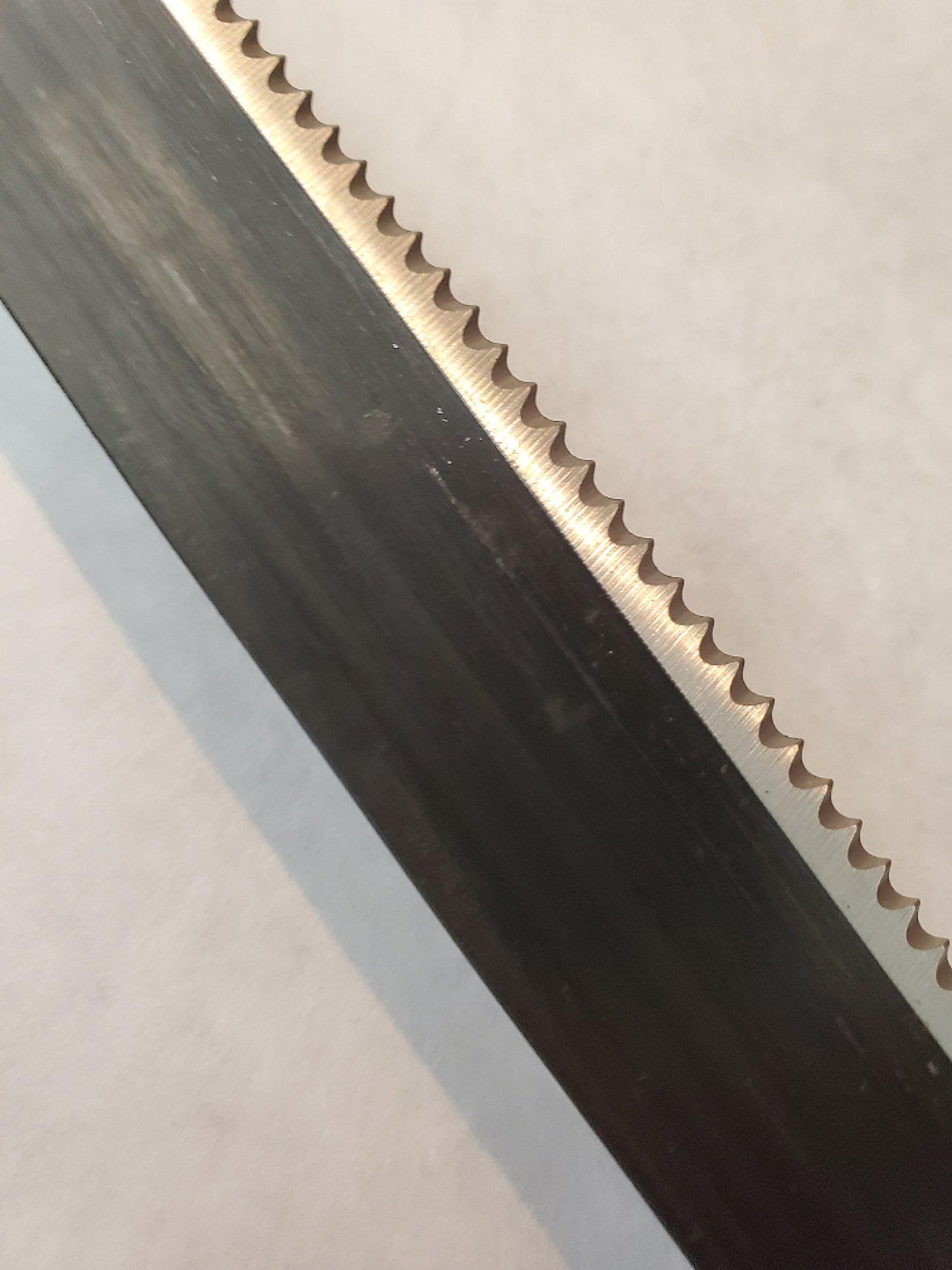 Close-up of a metal strip with teeth on one end and a smooth edge on the other, on a light gray background.
