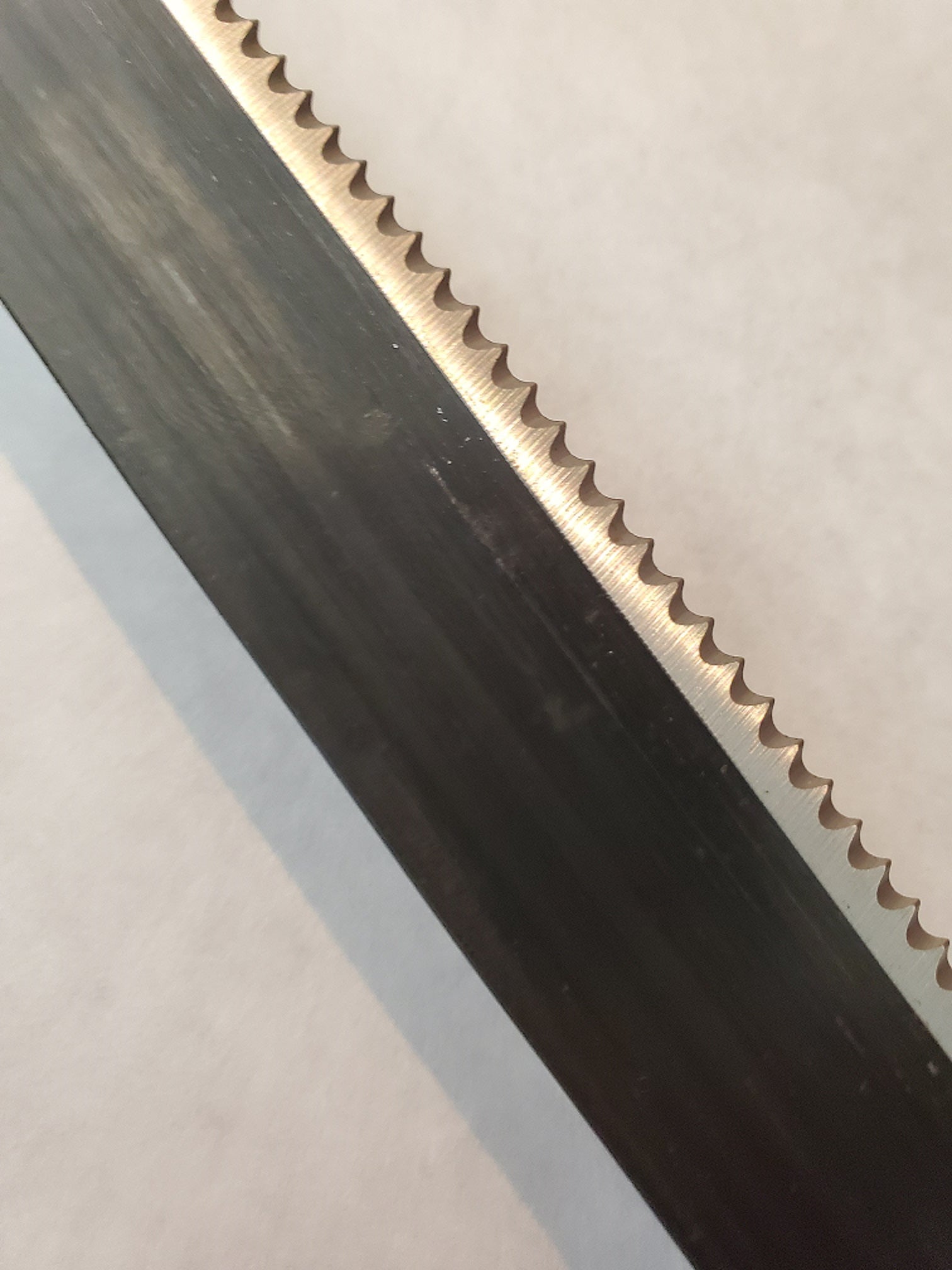 Close-up of a metal strip with teeth on one end and a smooth edge on the other, on a light gray background.